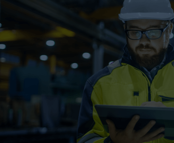 Man in hard hat troubleshooting something on a tablet in a manufacturing facility