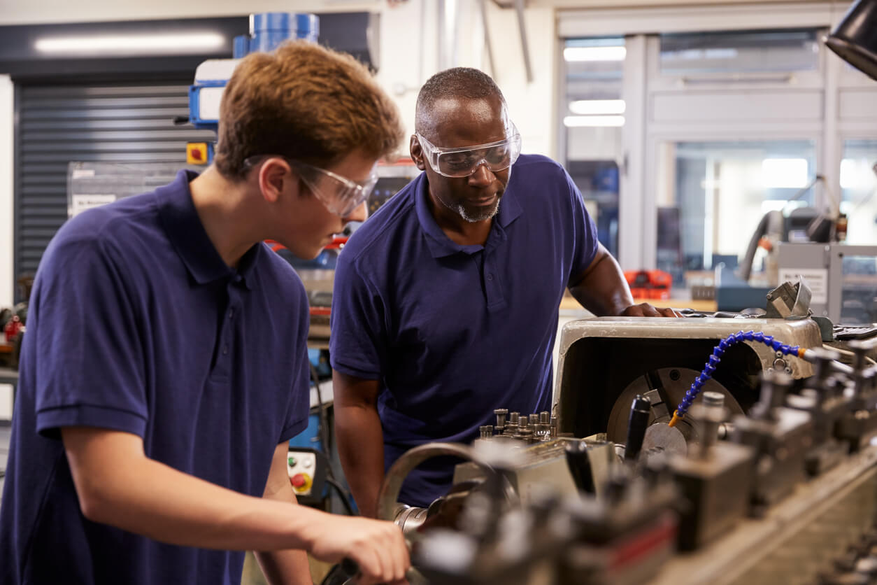 older team member teaching younger team member about a machine